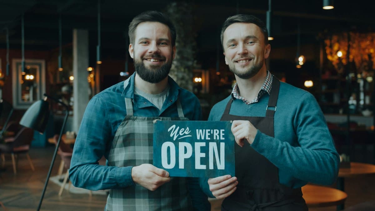 Two local business owners holding a We're Open sign
